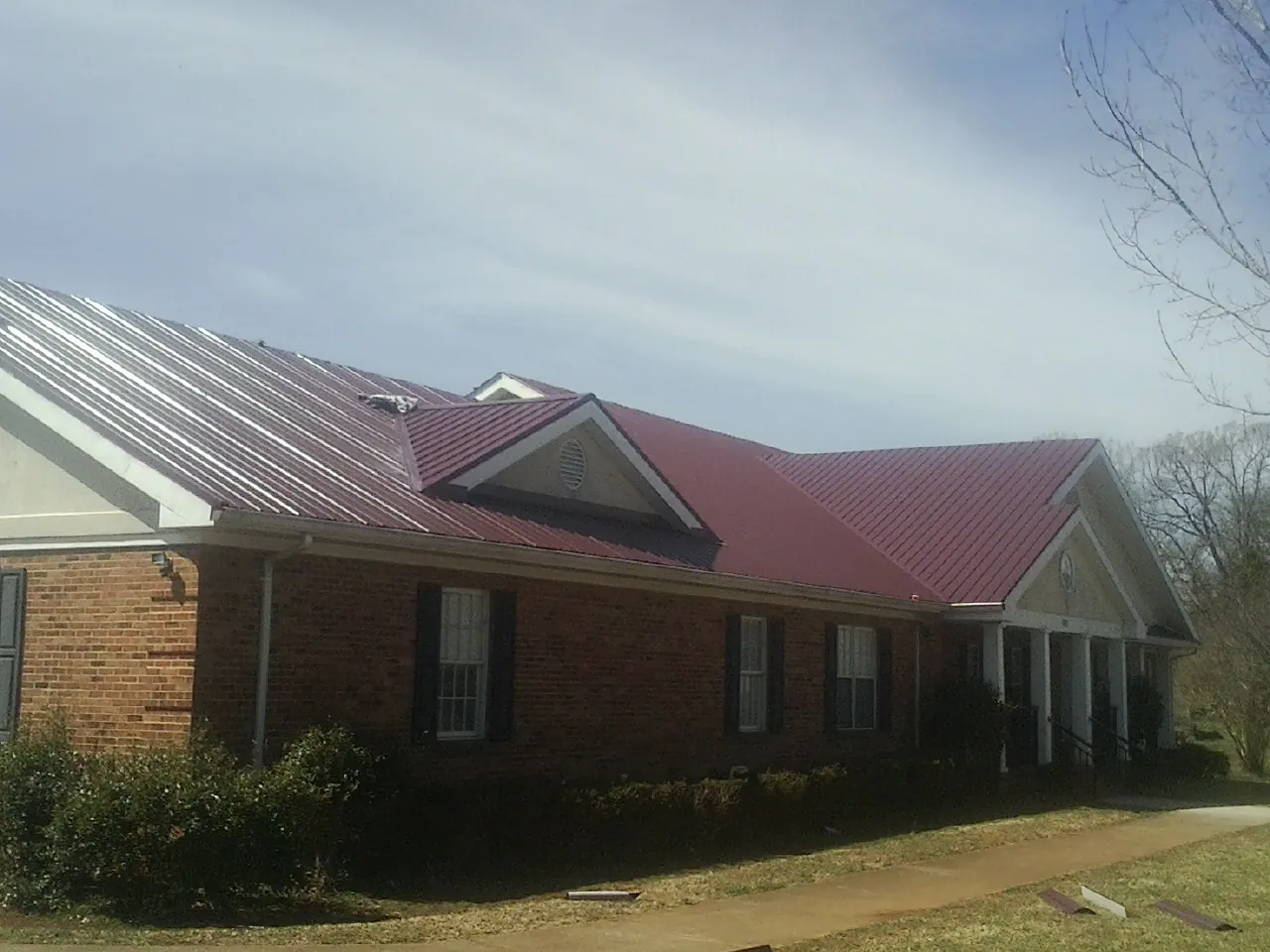 Red metal roof with gabled entries on a long brick building, from a Hail Damage Roof Repair job in Woodward