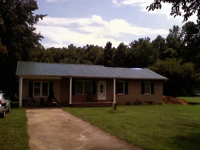 Dark green metal roof on a brick ranch with a covered porch in Woodward