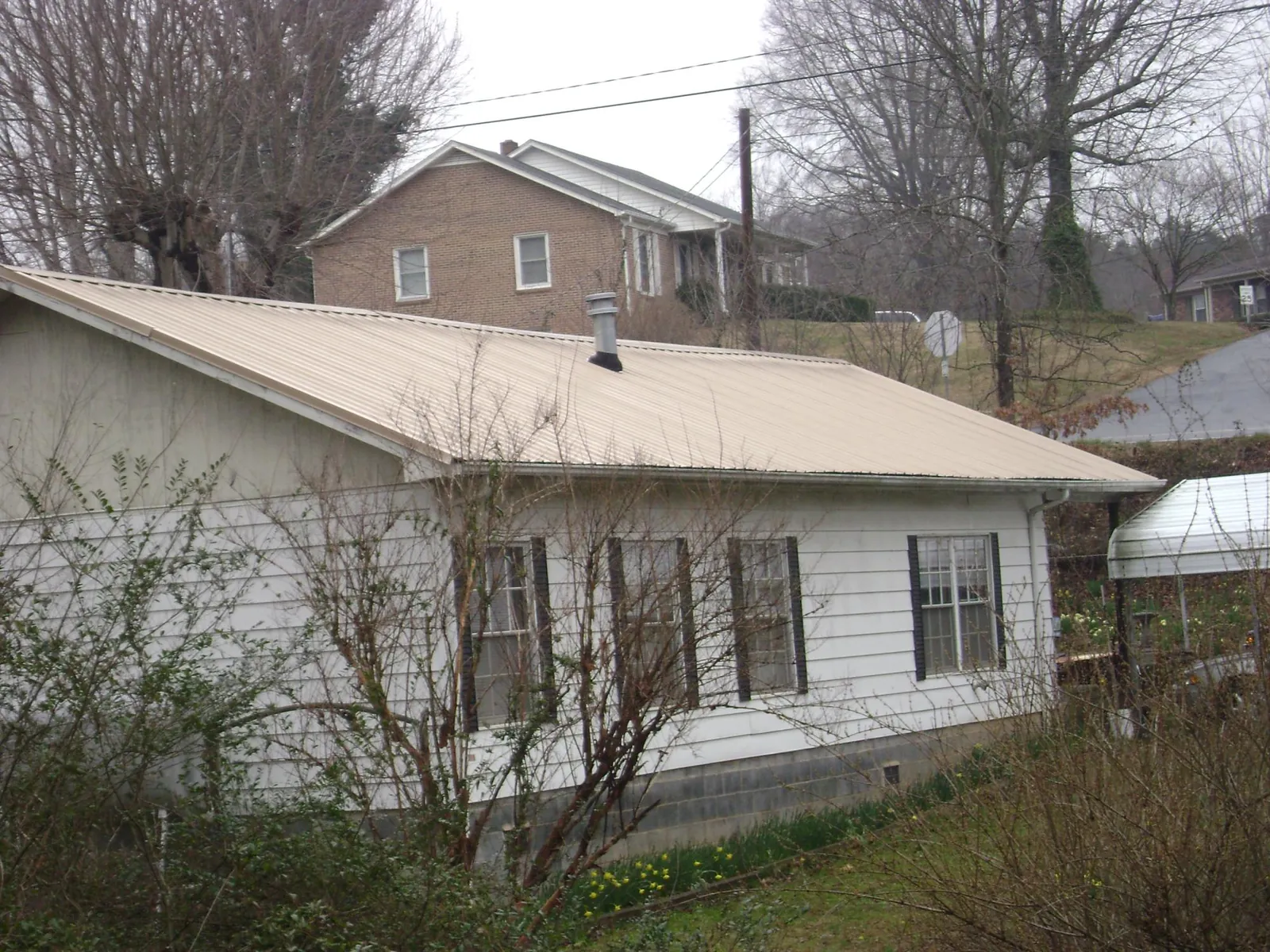 Tan metal roof on a white sided house set into a hillside — Commercial Roofing by Roofing Brothers in Woodward